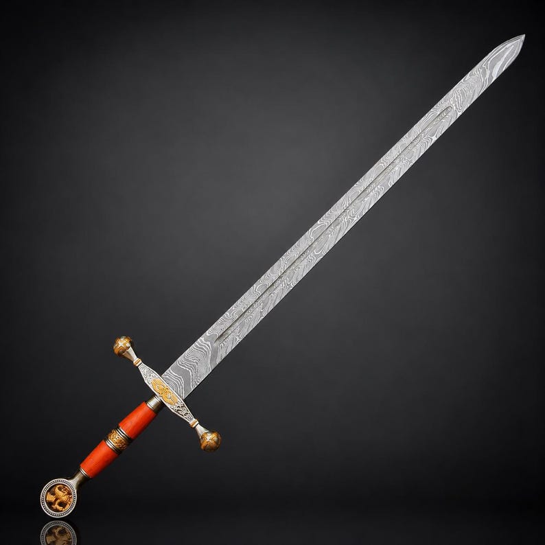 May include: A long sword featuring a double-edged blade with a distinct wavy Damascus steel pattern. The hilt includes a bright orange grip, a gold-toned crossguard with intricate engravings, and a circular pommel displaying a relief lion emblem.