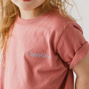 May include: A pink t-shirt with the name "Caroline" embroidered on the front in a silver thread.