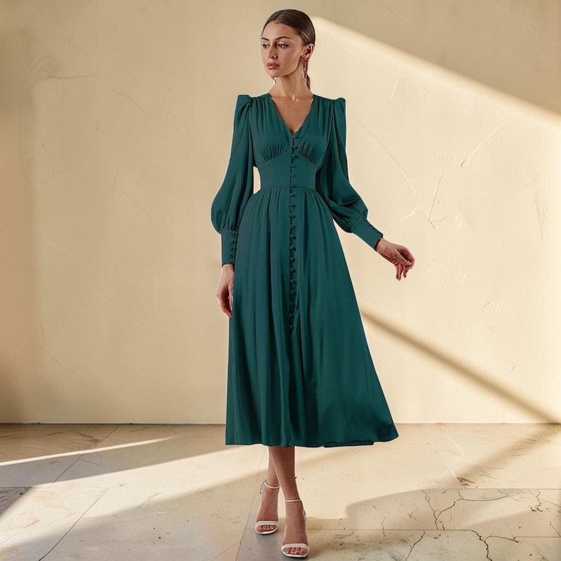 Puede incluir: Un vestido largo de color verde oscuro con escote en V y mangas largas. El vestido presenta una botonadura frontal y una cintura entallada. Las mangas son abullonadas en los hombros y se estrechan en las mu&ntilde;ecas. El vestido se combina con tacones blancos.