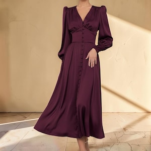 Puede incluir: Vestido largo de sat&eacute;n burdeos con escote en V y mangas largas. El vestido presenta una botonadura frontal y una cintura entallada. La falda llega hasta la pantorrilla. El vestido est&aacute; hecho de una tela brillante y suave.