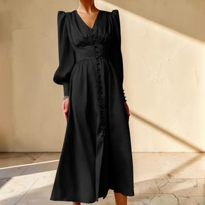 Puede incluir: Un vestido midi negro con escote en V y mangas largas. El vestido presenta una fila de botones en la parte delantera y una cintura entallada. Las mangas tienen un dise&ntilde;o de hombros abullonados. El vestido est&aacute; hecho de una tela suave y fluida.