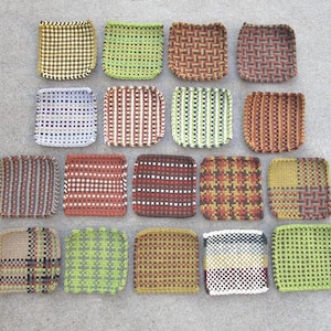May include: A collection of woven square coasters in various colors and patterns. The coasters feature designs such as gingham, stripes, and geometric shapes. Colors include green, red, brown, and blue. The coasters are arranged on a gray surface.