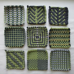 May include: Nine square woven potholders arranged in a grid, featuring various geometric patterns in shades of dark green, light green, gray, and white. Each potholder is constructed from thick, interlocking fabric loops with a textured finish.