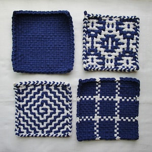 May include: Four square potholders arranged in a grid. One is solid navy blue, one features a white and navy blue geometric pattern, one has a white and navy blue diamond spiral design, and one displays a white and navy blue grid pattern.