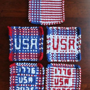 Könnte beinhalten: Gewebte quadratische Topflappen in Rot, Weiß und Blau. Ein Topflappen zeigt Streifen, während andere "USA", "1776" und "2026" in Weiß anzeigen. Die Kanten sind mit einem geflochtenen Rand versehen.
