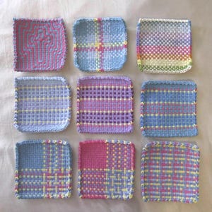 Pode incluir: Nove bases para copos quadradas tecidas com vários padrões. As bases apresentam uma mistura de cores pastel, incluindo rosa, azul, amarelo e roxo. Cada base tem um design único, com padrões geométricos e listras.