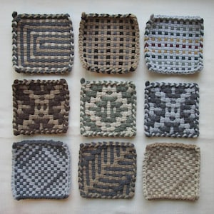 May include: A collection of nine square potholders arranged in a grid. Each potholder features a unique woven pattern in various neutral color palettes, including shades of brown, gray, beige, and black, with distinct braided edges on each piece.
