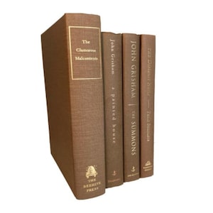 May include: A set of four brown hardcover books with gold lettering. The titles are "The Clamorous Malcontenti", "A Painted House", "The Summons", and "The Street Lawyer".