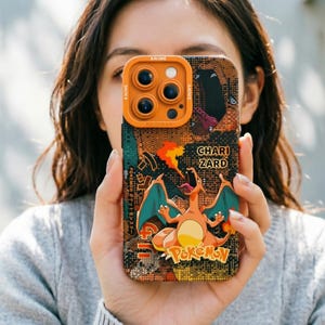 Op de afbeelding: Een telefoonhoesje met een Charizard-ontwerp uit de Pokemon-serie. De hoes heeft een oranje camerabult en een kleurrijk ontwerp met de woorden "Pokemon" en "Charizard". De hoes heeft een textuur, patroon achtergrond.