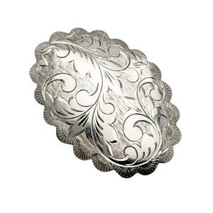May include: Oval-shaped silver-toned metal buckle with a scalloped edge. The buckle features an engraved floral design across its surface. The design is symmetrical and detailed, with swirling leaves and vines. The background is textured.