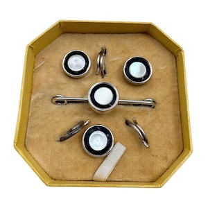 Può includere: Un set vintage di gemelli e bottoni per camicia in una scatola ottagonale gialla. I gemelli e i bottoni hanno un bordo nero con un centro bianco. Il set include due paia di gemelli, due bottoni per camicia e una barra per cravatta.