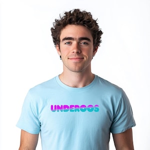 May include: A light blue t-shirt with the word "UNDEROOS" in a gradient of purple and teal. The shirt is worn by a person with curly brown hair and a neutral expression, against a white background.