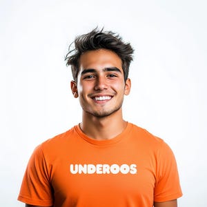 May include: An orange t-shirt with the word "UNDEROOS" in white block letters. The t-shirt is worn by a person with dark hair and a smile, set against a white background.