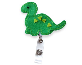 May include: Green felt dinosaur badge reel with yellow accents. The reel is attached to a white plastic clip.