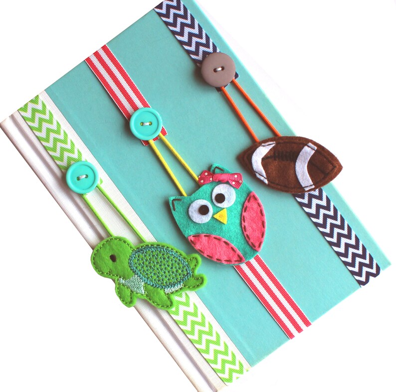 May include: Three felt bookmarks with different designs: a green turtle, a teal owl with pink accents, and a brown football. Each bookmark has a ribbon and a button.