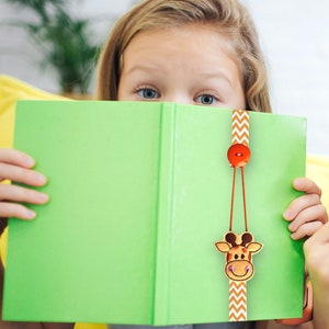 May include: A green book with a brown and orange giraffe bookmark. The bookmark has a red button and a chevron pattern.