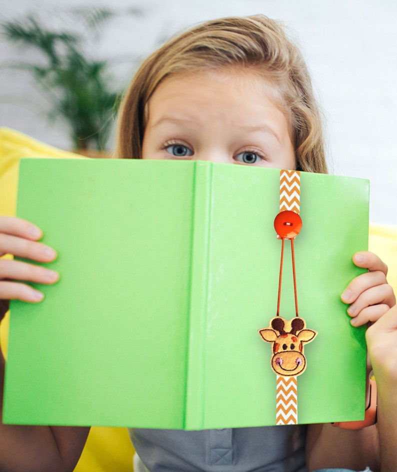 May include: A green book with a brown and orange giraffe bookmark. The bookmark has a red button and a chevron pattern.