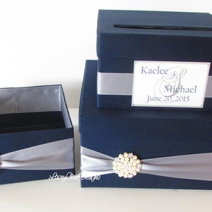 May include: Two navy blue wedding card boxes with silver ribbon and pearl embellishments. The top box has a slot for cards and a personalized label that reads "Kaelee & Michael June 20, 2015".