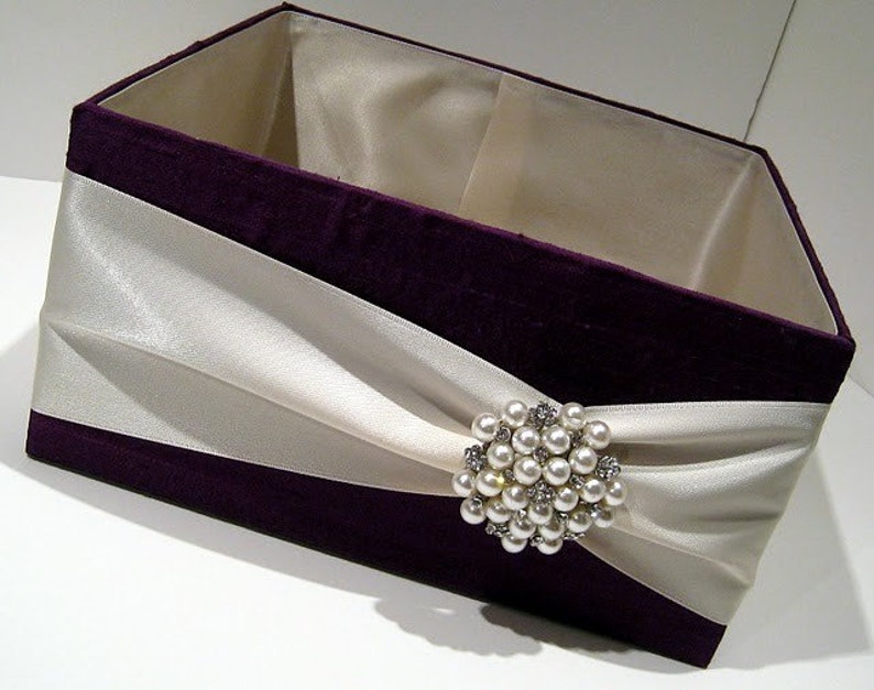 May include: A purple velvet box with a white satin ribbon and a pearl and rhinestone brooch.