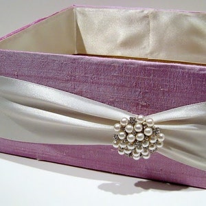 May include: A lavender-coloured gift box with a white satin ribbon and a pearl and rhinestone brooch.