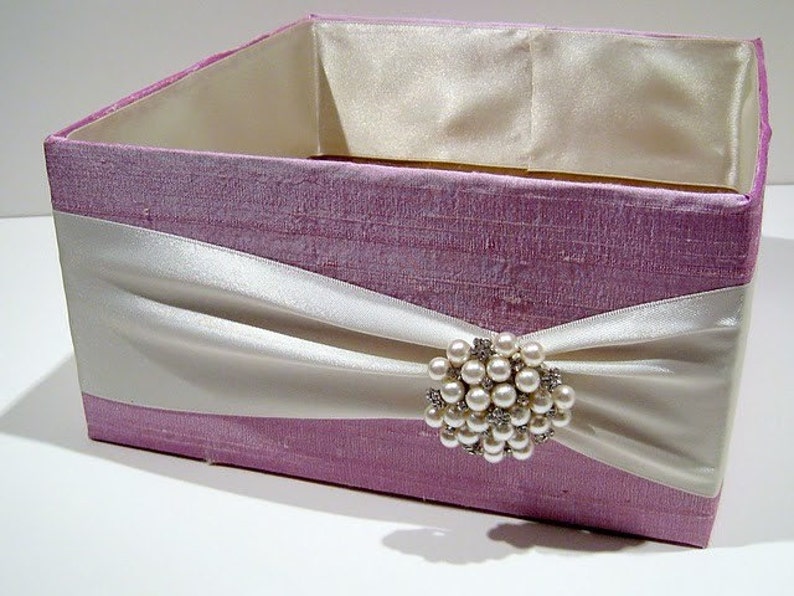 May include: A lavender-coloured gift box with a white satin ribbon and a pearl and rhinestone brooch.