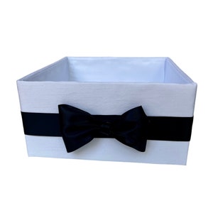 May include: A white fabric storage box with a black satin ribbon tied in a bow.
