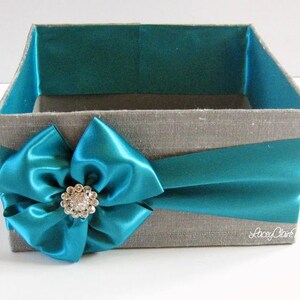 May include: A gray fabric gift box with a teal satin ribbon and bow. The bow has a large rhinestone embellishment in the center. The box is empty.