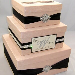 May include: Three-tiered blush-colored card box set with black ribbon accents and rhinestone embellishments. The top box has a slot for cards. The middle box features a nameplate that reads "Tia & Barry December 22, 2012."