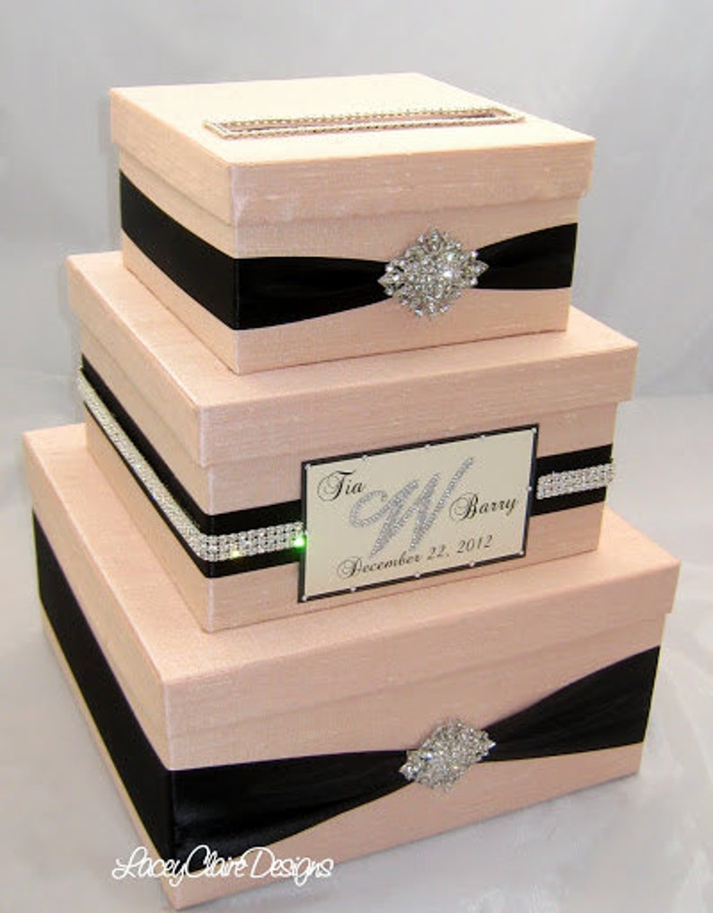 May include: Three-tiered blush-colored card box set with black ribbon accents and rhinestone embellishments. The top box has a slot for cards. The middle box features a nameplate that reads "Tia & Barry December 22, 2012."