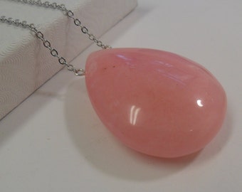 May include: A pink teardrop-shaped pendant necklace. The pendant is a solid, glossy pink color and is suspended from a delicate silver chain. The necklace is displayed on a white surface.