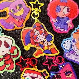May include: A selection of cartoon character keyrings in various colours. Each keyring showcases a distinct design with bright colours and glitter details. The keyrings are attached to star-shaped clasps.