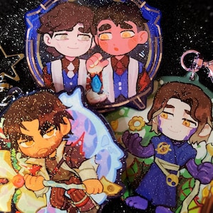 May include: A collection of colorful acrylic charms featuring cartoon illustrations of characters. The charms have various shapes, including a star and circular designs. Each charm has a metal clasp for attachment. The characters are depicted in various outfits and poses.