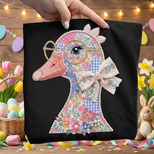 May include: Black tote bag featuring a whimsical goose design. The goose is adorned with glasses, a bow, and floral patterns in pink, blue, and white. The design is embellished with pearls and floral accents, creating a charming, decorative aesthetic.