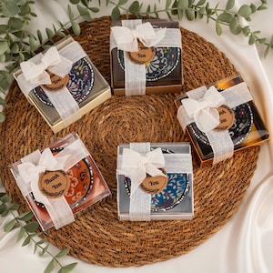 Op de afbeelding: Vijf kleine, decoratieve keramische schaaltjes met kleurrijke patronen, elk verpakt in een transparante doos en vastgebonden met een wit lint en een "Thank You" label. De schaaltjes liggen op een geweven, cirkelvormige mat.
