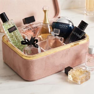 Puede incluir: Un estuche de tocador de terciopelo rosa con borde dorado que contiene varios frascos de perfume de vidrio, incluyendo Valentino, Prada, J'adore, Aqva Pour Homme, Sauvage, Joy y YSL. Los frascos presentan diversas formas y tapones.