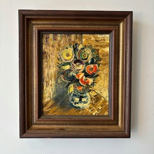 Pode incluir: Pintura a óleo de um arranjo floral num vaso azul e branco, sobre um fundo texturizado. As flores são em tons de amarelo, laranja e roxo. A pintura está numa moldura de madeira castanha escura.