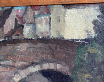 May include: An oil painting on canvas featuring a stone bridge with a dark archway, set against a backdrop of buildings with cream, brown, and red tones. The artwork is enclosed in a simple wooden frame with a visible grain and textured surface.