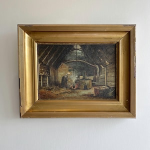 Pode incluir: Uma pintura a óleo numa moldura dourada larga e ornamentada, representando uma cena interior rústica. Uma figura com vestes escuras e um toucado claro está junto a um pequeno fogo num chão de terra, com paredes de madeira e telhado de colmo.