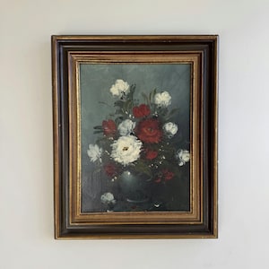 Può includere: Un dipinto a olio in una cornice marrone scuro e oro raffigurante una composizione floreale con fiori bianchi e rossi in un vaso scuro su uno sfondo grigio-verde tenue. La composizione presenta pennellate visibili e consistenza.