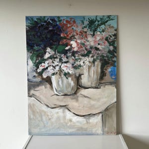 Op de afbeelding: Olieverfschilderij van twee witte vazen ​​gevuld met kleurrijke bloemen. De bloemen zijn een mix van wit, roze en rood, met donkerblauwe en groene bladeren. De vazen ​​staan ​​op een wit tafelkleed, met een lichtblauwe achtergrond.