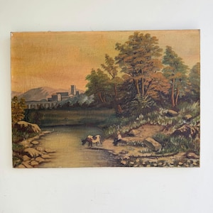 Pode incluir: Uma pintura a óleo sobre tela retratando uma paisagem com um rio, uma pessoa sentada na margem e um burro a pastar. Ao fundo, há árvores, montanhas e uma estrutura de pedra com arcos sob um céu de tons dourados.