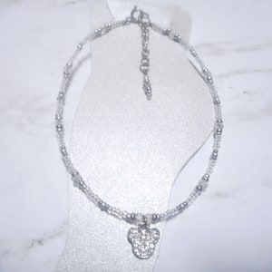 May include: A silver anklet with a clear bead strand and small silver beads. The anklet features a pendant in the shape of a mouse head, encrusted with clear rhinestones. The anklet is displayed on a white foot form.