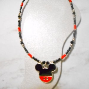 Pode incluir: Um colar de contas com um pingente do Mickey Mouse. O colar tem contas pretas e vermelhas com detalhes dourados. O pingente do Mickey Mouse &eacute; preto com uma base vermelha e uma borda prateada.