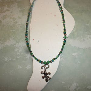 May include: A green and silver ankle bracelet with a silver lizard charm.