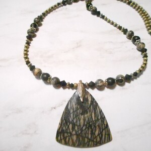 May include: A necklace with a large triangular pendant made of black and brown stone with a gold leaf charm. The necklace is made of black and brown beads.