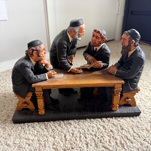 Könnte beinhalten: Eine dekorative Figur mit vier bärtigen Personen, die dunkle Käppchen und schwarze Anzüge tragen und um einen Holztisch sitzen oder stehen. Eine Figur hält ein offenes Buch, während die anderen gestikulieren, alles auf einem rechteckigen Sockel.