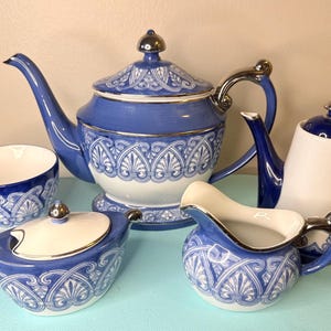 May include: A blue and white porcelain tea set with a decorative pattern. The set includes a teapot, creamer, sugar bowl, cup, and a second teapot. The handles and lids have silver accents.