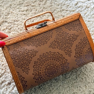 May include: A vintage brown handbag with a decorative pattern. The rectangular bag has a handle and a clasp closure. The frame and handle are a lighter brown, while the body of the bag features a darker, embossed design.