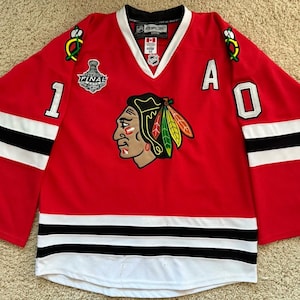 May include: Red hockey jersey with black and white accents. Features the number 1 and the letter A. Includes a team logo and the word "FINAL". The jersey has a V-neck and the NHL logo.