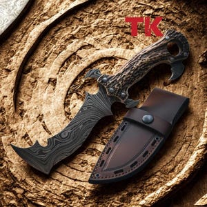 Può includere: Un coltello decorativo con una lama curva e seghettata e un manico strutturato. La lama ha un design scuro e modellato e il manico ha un aspetto marrone, simile a quello del corno. Include un fodero in pelle marrone. Il testo "TK Traditional Knife" è visibile.